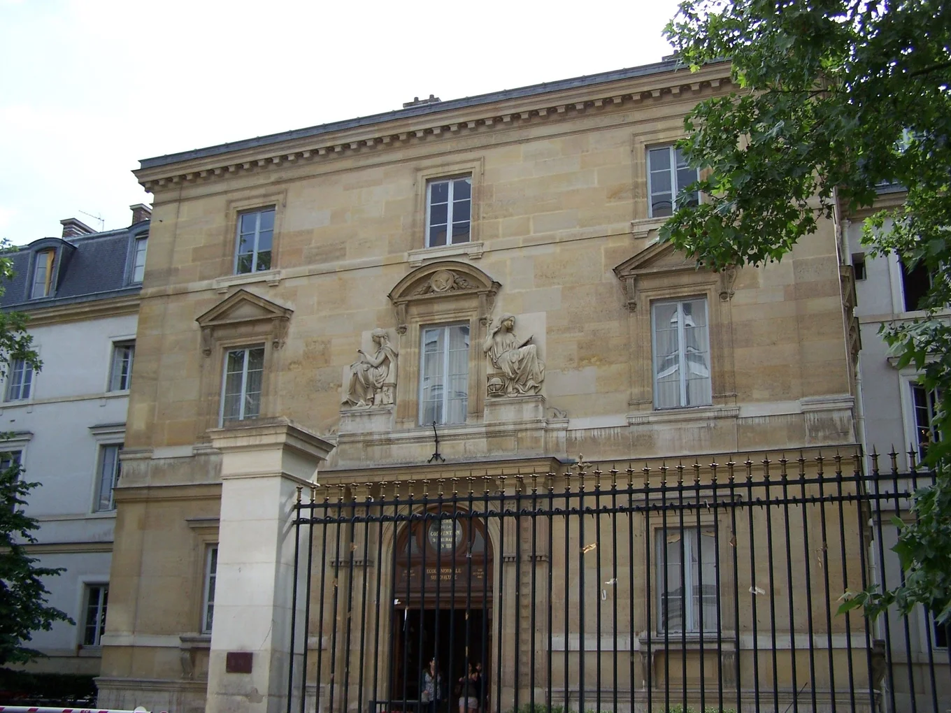 Historic building, gated entrance, sculptures, windows.
